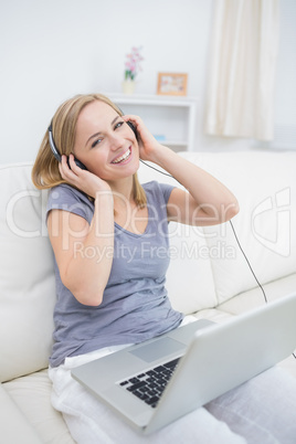 Happy woman listening music through headphones with laptop