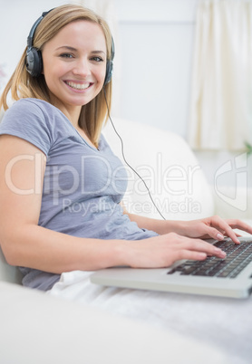 Woman listening music through headphones while using laptop