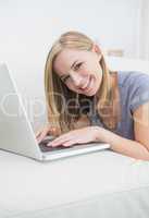 Portrait of casual woman lying on couch and using laptop