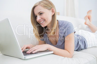 Casual woman lying on couch and using laptop