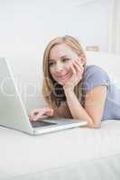 Casual woman lying on couch and using laptop