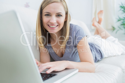 Portrait of casual woman lying on couch and using laptop