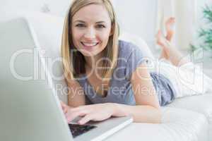 Portrait of casual woman lying on couch and using laptop