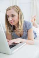 Casual woman lying on couch and using laptop