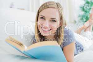 Portrait of happy woman with storybook lying on couch