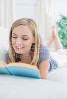 Young woman reading book lying on couch