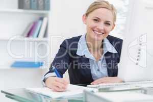 Smiling business woman writing notes at office desk