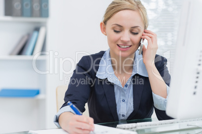 Business woman writing while on call at desk in office