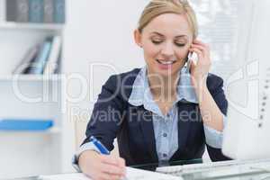 Business woman writing while on call at desk in office