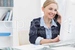 Happy business woman using computer while on call at desk