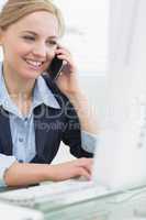 Happy business woman using computer while on call at desk