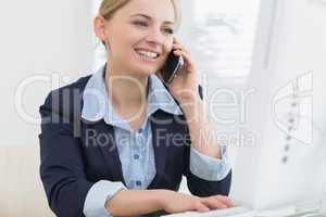 Happy business woman using computer while on call at desk