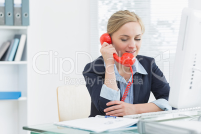 Female executive using red land line phone at desk