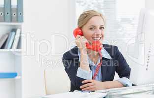 Smiling female executive using red land line phone at desk