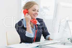 Female executive using red land line phone at desk