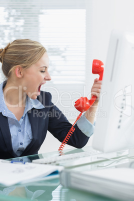 Female executive yelling into red telephone receiver at desk