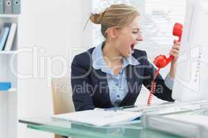 Female executive yelling into red telephone receiver at desk