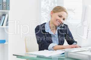 Female executive using landline phone and computer at desk