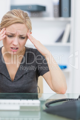 Business woman rubbing her temples at office desk