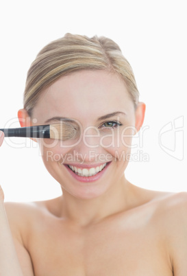 Close-up of playful woman covering eye with make-up brush