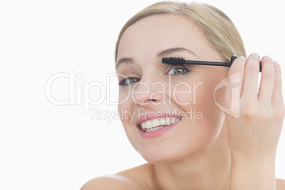 Close-up portrait of young woman applying mascara to her eye