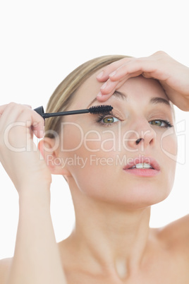 Close-up portrait of young woman applying mascara to her eye