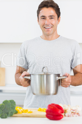 Man holding large pot in front of chopping board with vegetables