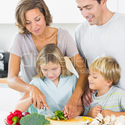 Mother teaching daughter to slice vegetables as father and son a