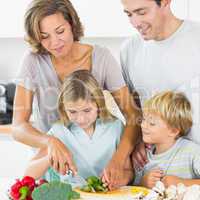 Mother teaching daughter to slice vegetables as father and son a