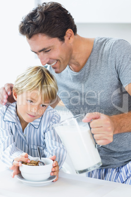 Smiling father pouring milk for sons cereal