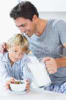 Smiling father pouring milk for sons cereal
