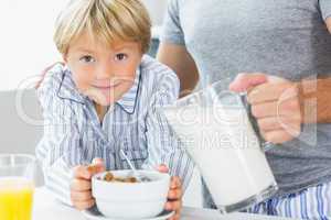 Father pouring milk for sons cereal