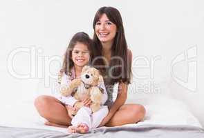 Mother and daughter sitting on bed with teddy bear