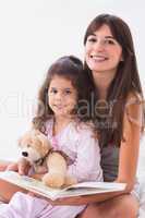 Mother and daughter reading together with teddy bear