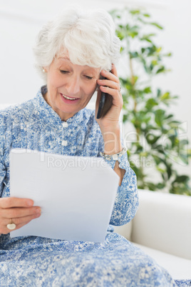 Elderly happy woman reading a paper on the phone