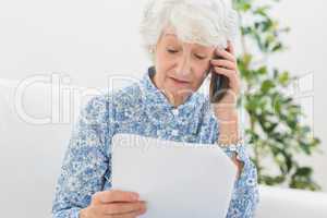 Elderly woman reading papers on the phone
