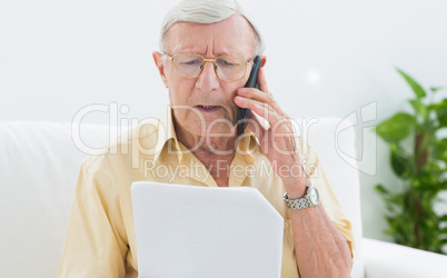 Elderly man reading papers on the phone