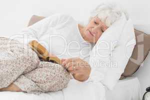 Old woman lying on the bed and reading