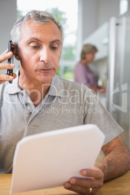 Focused mature man calling with a sheet of paper