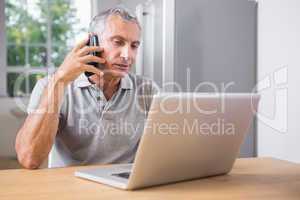 Mature man using his laptop and calling