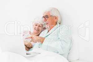 Happy couple using laptop in bed