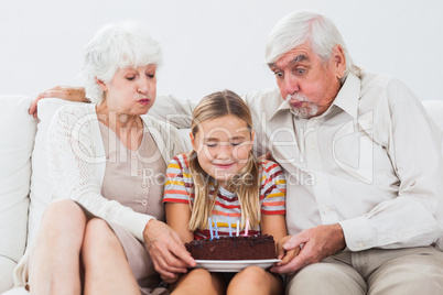 Little girl and grandparents blowing out the candles