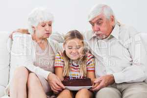 Little girl and grandparents blowing out the candles