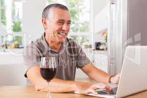 Happy man using laptop with glass of red wine