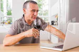 Smiling man drinking red wine and looking at laptop