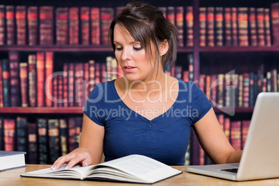 Woman reading book with computer