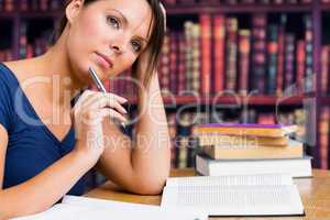 Woman thinking with pen and book in library