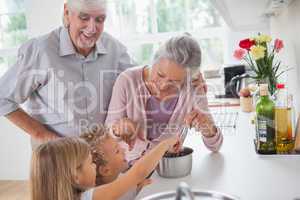 Smiling grandparents helping children to cook