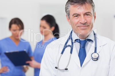 Doctor with stethoscope smiling and his team behind him