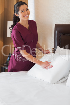 Smiling hotel maid making bed